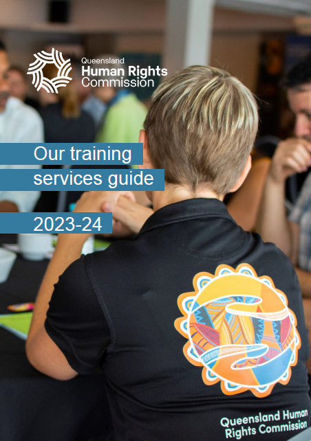 Close up colour photo of a person with a black polo shirt and short blond hair sitting at a table with several other people. Everyone else is out of focus. The polo shirt has the name and logo of the Queensland Human Rights Commission on the back. 