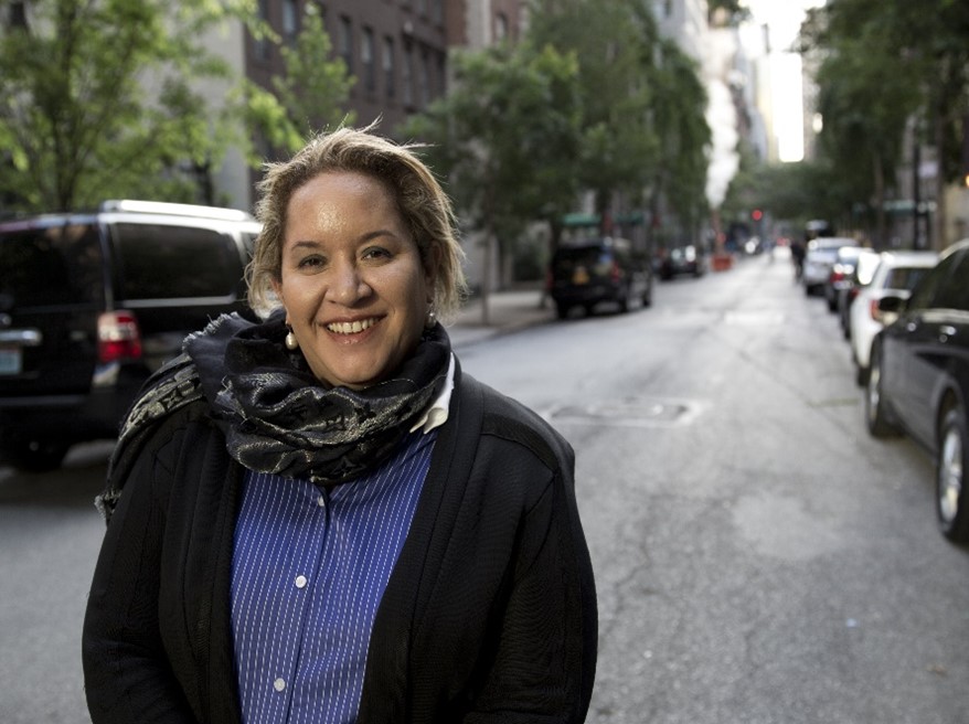 Professor Dr Megan Davis, standing on a city street. She's wearing a blue shirt and black jacket and scarf, and is smiling.