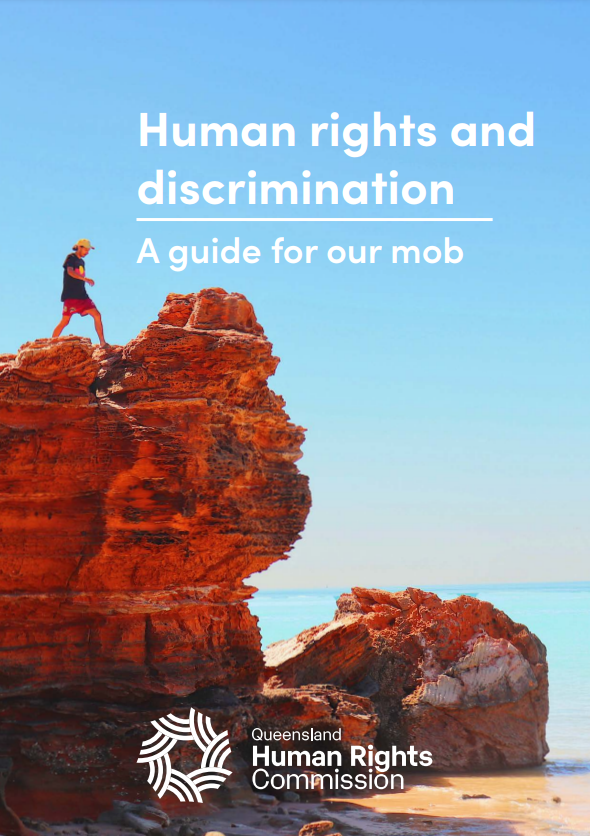 The cover of this guide is a photo of a beach. The water is pale blue and very calm. It is a clear day and the sky is also pale blue. There is a large crop of red rock close to the water. A young man is climbing along the top of it, wearing red shorts, a yellow cap, and a black shirt with the Aboriginal flag on the front. White text across the photo reads 'Human rights and discrimination: a guide for our mob.' The QHRC logo is at the bottom of the image. 